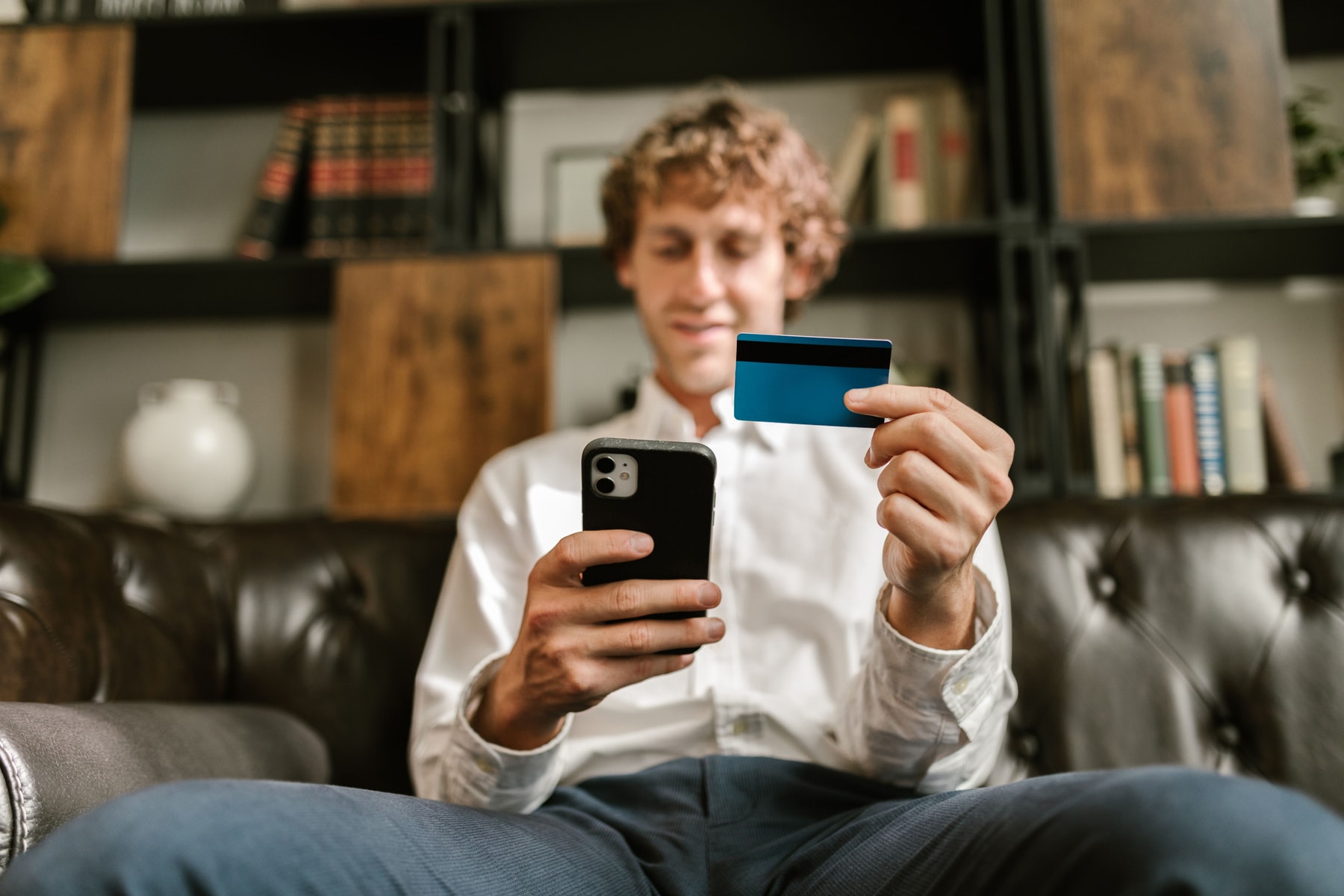A man on a sofa holding a bank card and a phone